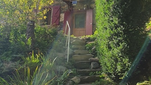 Un escalier en pierre menant à une porte en bois, entouré d’une végétation luxuriante et d’un mur de pierre.