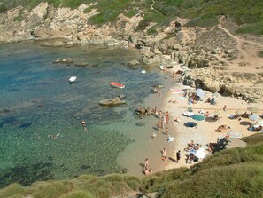 Een kuststrand met helder water, rotsachtig terrein en mensen die zonnebaden.