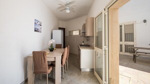 Una cucina funzionale con frigorifero, fornelli e microonde. È presente un tavolo da pranzo con sedie e una ventola a soffitto.