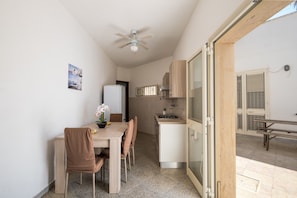 Una cocina compacta con refrigerador, estufa y microondas. Cuenta con una mesa de comedor con sillas y un ventilador de techo.