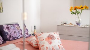 Una camera da letto con un letto rosa, cuscini floreali, una cassettiera e un vaso con girasoli.