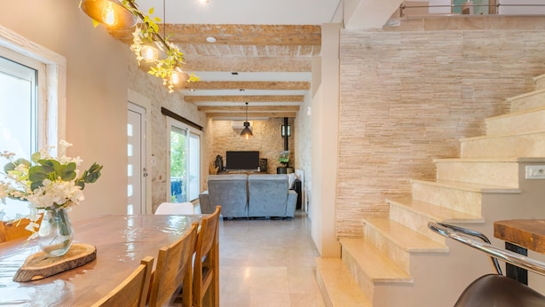 Uma cozinha moderna com painel de pedra, uma área de jantar com mesa e cadeiras de madeira e uma escada com corrimão de metal.