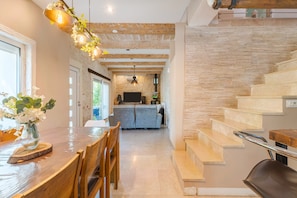 Une cuisine moderne avec un mur de protection en pierre, un coin repas avec une table et des chaises en bois, et un escalier doté d’une rampe en métal.