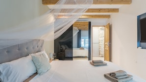 Quarto com cama, mesa de cabeceira, luminária, janela e porta que dá para outro cômodo.