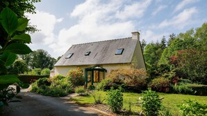 A house with a sloped roof, a small porch, and a garden with various plants and shrubs.