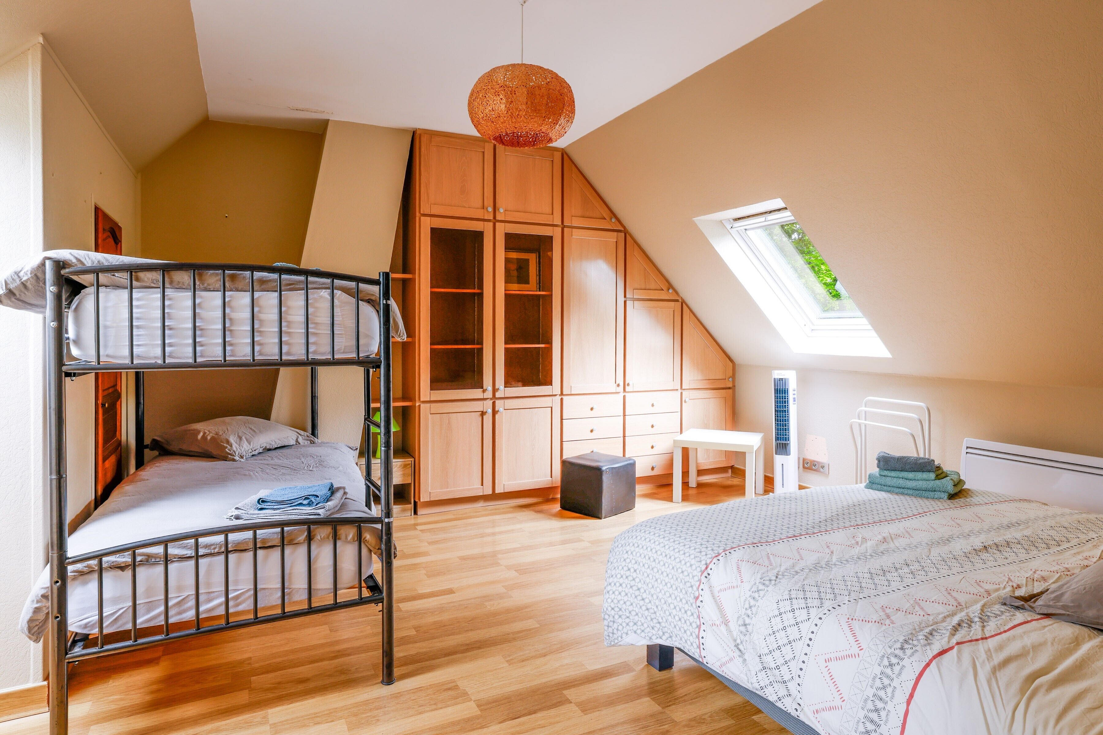 Une chambre de type dortoir, équipée de lits superposés, d’un bureau, d’une chaise, d’une armoire et d’une lucarne.