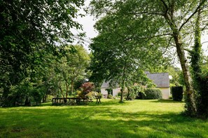 A garden with a picnic table and a house in the background.