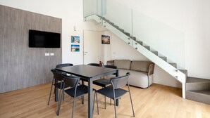 Un espace de vie moderne comprenant un coin repas, un canapé, un escalier et un téléviseur à écran plat fixé au mur.