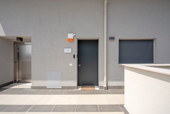 A modern building entrance with a grey door, a small mailbox, and a security camera.