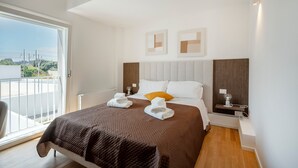 Une chambre d’hôtel avec un grand lit, une vue par une porte coulissante, une table de chevet avec une lampe et une œuvre d’art accrochée au mur.