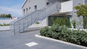 Un bâtiment moderne à la façade incurvée, doté d’un escalier en verre et agrémenté d’un espace paysager avec des arbustes.