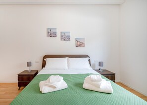 Una cama bien hecha con sábanas blancas, dos lámparas de noche y una colcha verde acolchada.