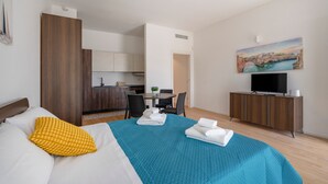 Quarto de hotel com cama, escrivaninha, mesa de jantar, televisão e um quadro na parede.