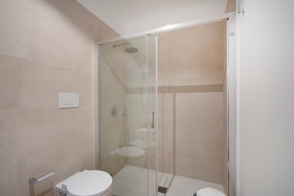 A modern bathroom with a glass-enclosed shower, a toilet, and a sink.