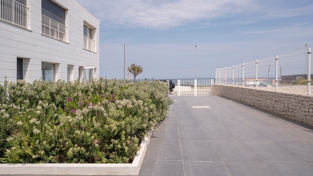 Um edifício moderno com um caminho pavimentado, um muro de pedra e uma cerca de metal.