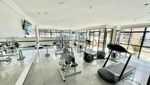 Une salle de sport équipée de divers appareils d’exercice, dotée de grandes fenêtres et d’un plancher plat.