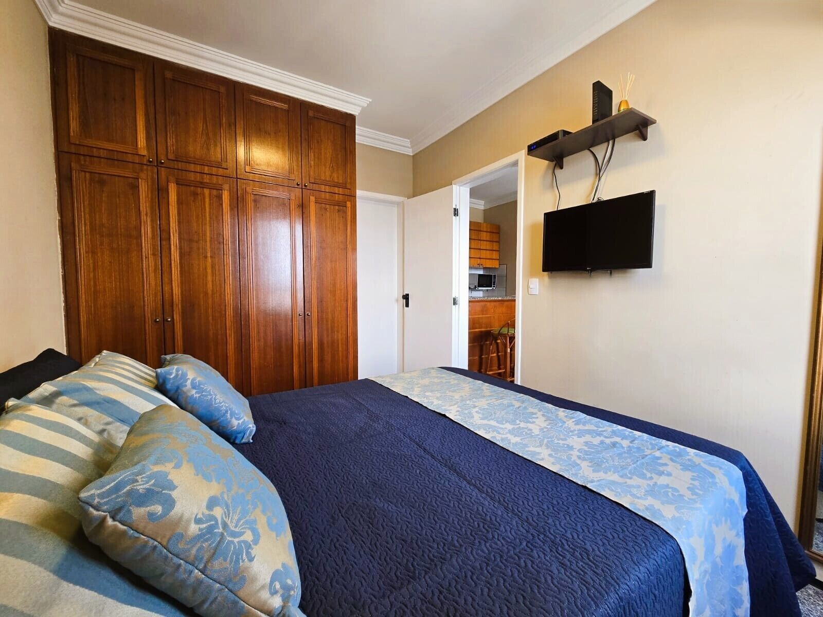 A bedroom with a bed, wooden wardrobe, and a TV on the wall.