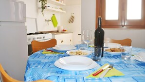 Une table à manger dressée avec des assiettes, des couverts et une bouteille de vin, avec une cuisine en arrière-plan.