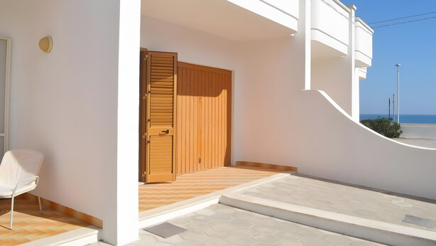 Un bâtiment blanc avec une porte en bois, une chaise blanche et une vue sur la mer.