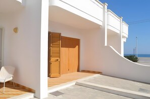 Un edificio blanco con puerta de madera, una silla blanca y vistas al mar.