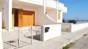 Un bâtiment blanc avec une porte en bois, une boîte aux lettres et une entrée fermée par un portail.