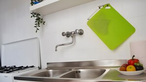 Une cuisine moderne avec un évier en acier inoxydable, une planche à découper verte et un saladier rempli de fruits.