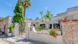 A residential building with a stone wall, potted plants, and a gate.