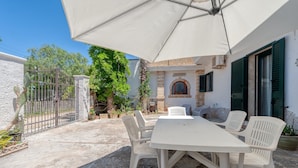 An outdoor patio with a white table and chairs, a white umbrella, and a stone wall.