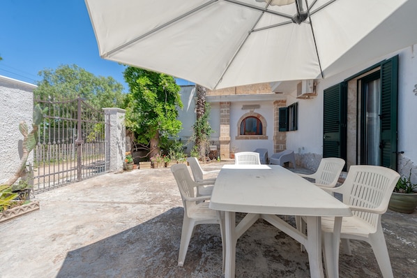 Une terrasse extérieure avec une table et des chaises blanches, un parasol blanc et un mur en pierre.