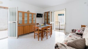 Un comedor con una mesa y sillas de madera, un televisor montado en la pared y un sofá estampado con motivos florales.