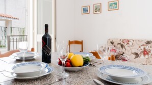Una mesa de comedor dispuesta con platos, vasos, una botella de vino y un bol de fruta.