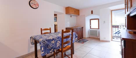 Un comedor con mesa y sillas, una cocina con armarios, un reloj y vistas a un balcón exterior.