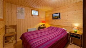 A wooden cabin room with a bed, a chair, a map on the wall, and a lamp on the nightstand.