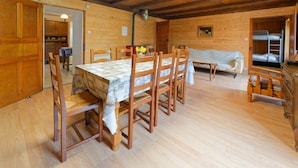 A wooden cabin interior with a dining table, chairs, a sofa, and a bunk bed.