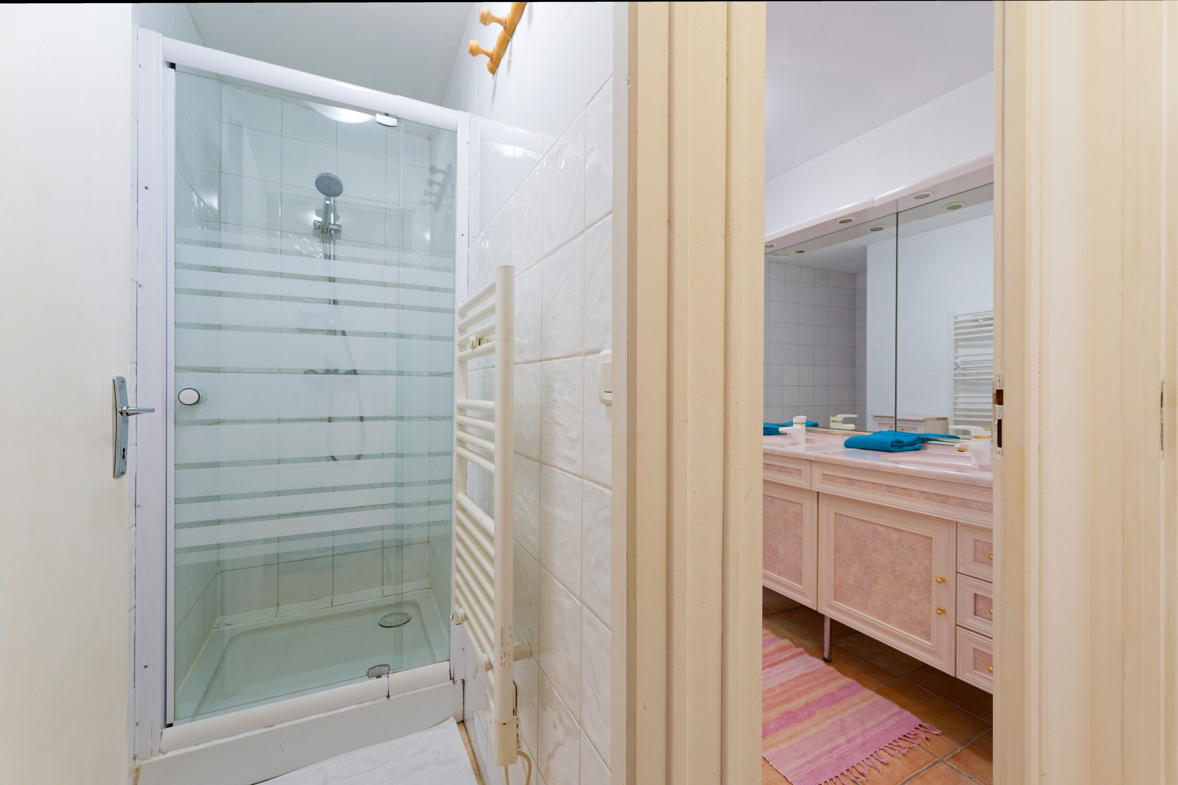 Un baño con ducha envuelta en cristal, un lavabo blanco con espejo y una alfombra rosa a rayas.