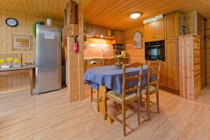 A wooden interior with a dining table, chairs, a refrigerator, a microwave, and wooden cabinets.