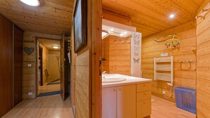 Interior de una cabaña de madera con baño que incluye un lavamanos, armarios y zona de ducha.