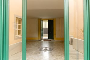A hallway with a marble floor, a door with a metal gate, and a window with bars.