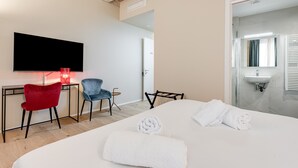 A hotel room with a bed, two chairs, a desk, a TV, and a bathroom with a sink.