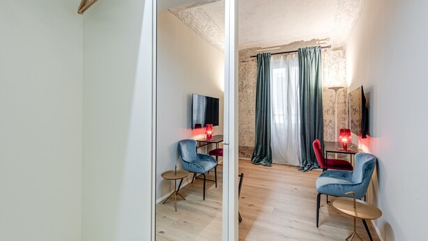 A room with a wooden floor, a dining table with chairs, a TV, and a red lamp.