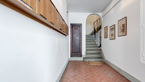Un couloir avec une armoire en bois, une porte sombre, un escalier et des tableaux encadrés accrochés au mur.
