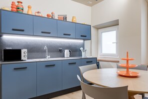 Une cuisine moderne avec des meubles bleus, un four à micro-ondes, une bouilloire et une table à manger avec des chaises.