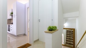 Um interior moderno com cozinha, tapete de boas-vindas, planta em vaso e escadaria de mármore.