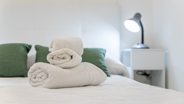 Cama arrumada com toalhas enroladas e abajur.