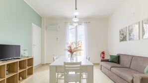 Uma sala de estar moderna com uma mesa de jantar branca, um sofá e uma televisão sobre uma estante de madeira.