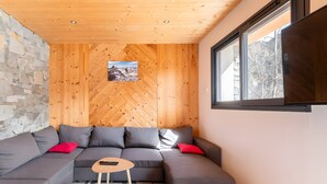 Een modern interieur met een houten plafond, een stenen muur en een grijze modulaire bank met rode kussens.