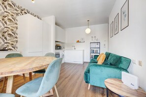 Une cuisine moderne avec des meubles blancs, une table à manger avec des chaises, un canapé vert et une petite table ronde sur laquelle se trouve un appareil.