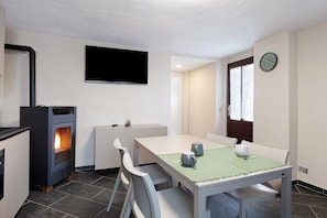 A dining area with a table, chairs, a TV, a fireplace, and a clock on the wall.