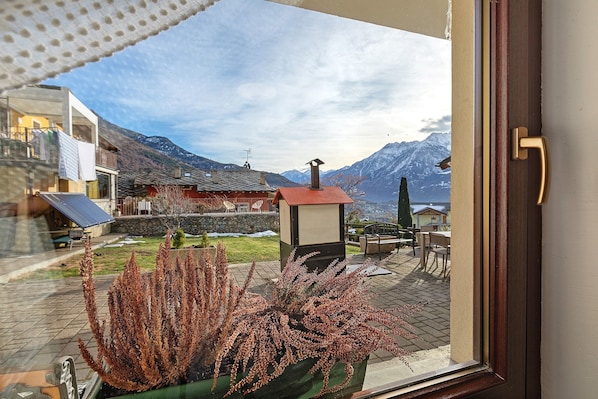 A window view of a mountain landscape with a building, a red-roofed structure, and a small kiosk.