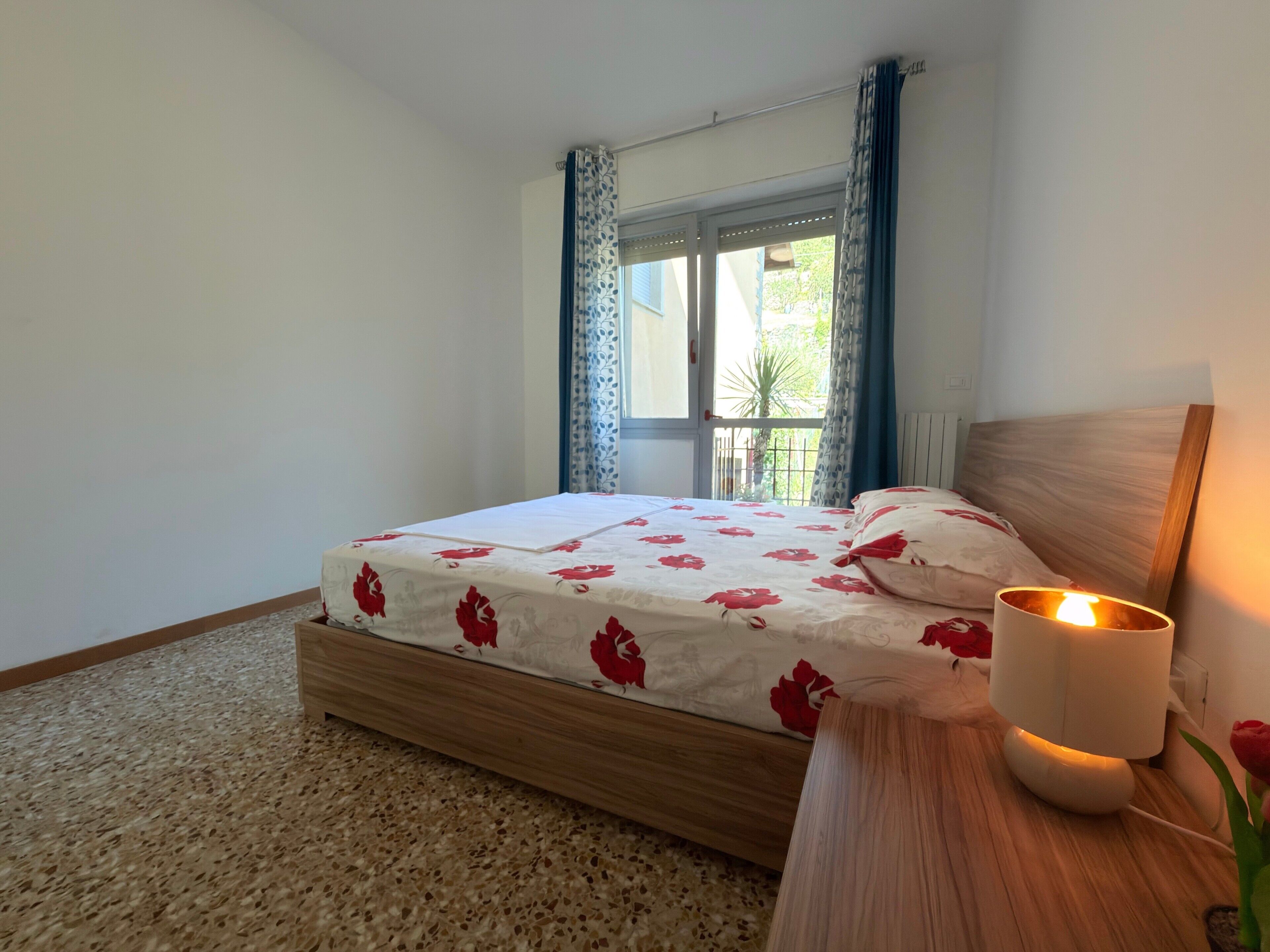 Ein Schlafzimmer mit einem Bett, einem Nachttisch mit Lampe und einem Fenster mit Vorhängen.